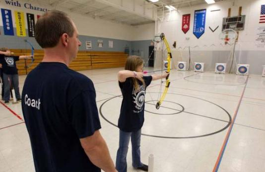A student pulls back on a bow as her MoNASP coach looks on.