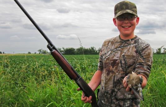 A young boy with a shotgun holds a dove he just harvested