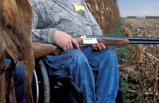 A dove hunter sits in a field with his shotgun.