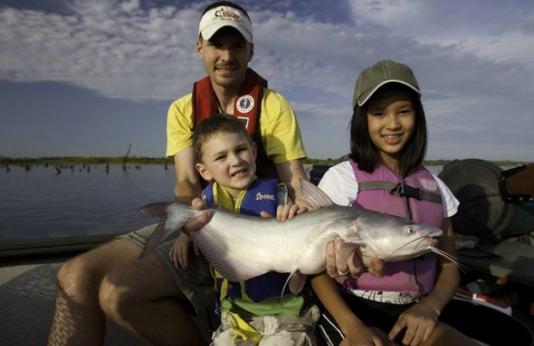 A father, son, and daughter pose with a catfish caught at a Missouri lake.