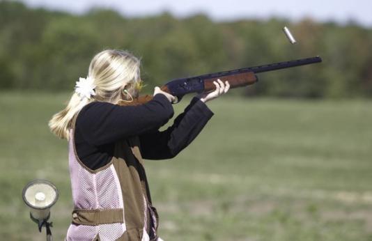 A woman aims her shotgun during target practice