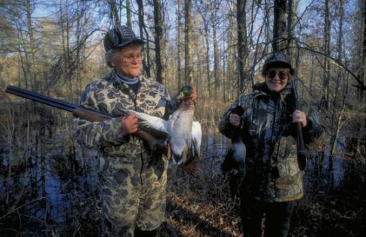 two women duck hunting with one holding a male mallard