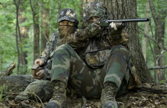 two turkey hunters in camo sitting against tree